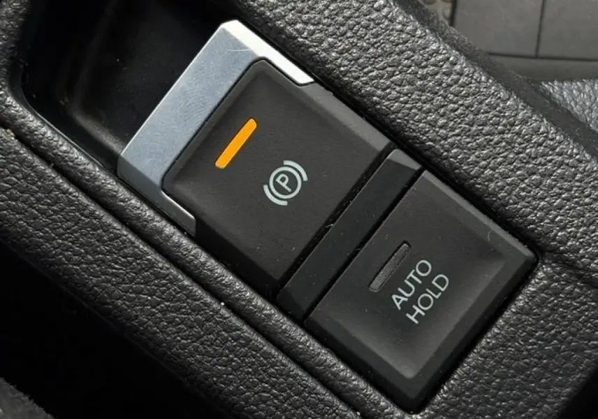 Gros plan sur le bouton de frein de stationnement électrique et fonction Auto Hold dans l’habitacle noir du Volkswagen T-Roc 2025.