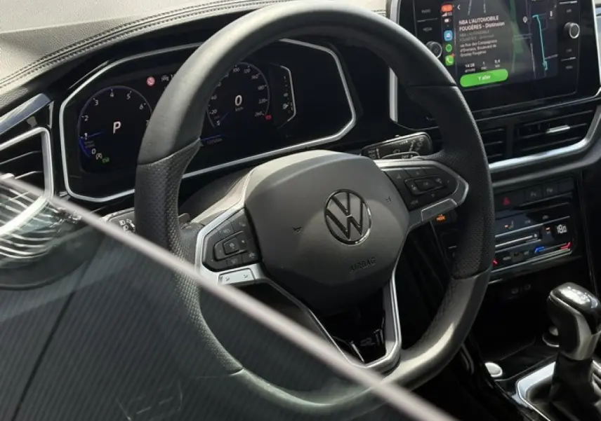 Vue rapprochée du volant multifonction noir et du tableau de bord digital du Volkswagen T-Roc 2025, avec écran tactile et levier de vitesse.