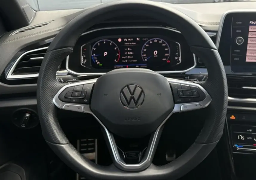 Vue rapprochée du volant cuir noir avec logo Volkswagen et tableau de bord digital du Volkswagen T-Roc 2025.