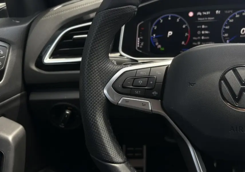 Gros plan sur le volant cuir perforé noir du Volkswagen T-Roc 2025 avec commandes multifonctions et tableau de bord digital.