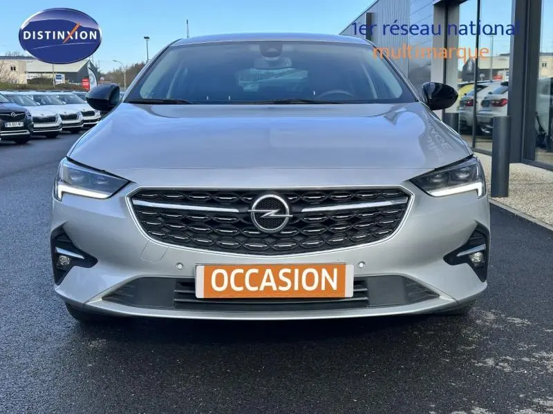 Vue frontale d'une Opel Insignia Grand Sport gris clair avec calandre noire et plaque "OCCASION" orange visible.