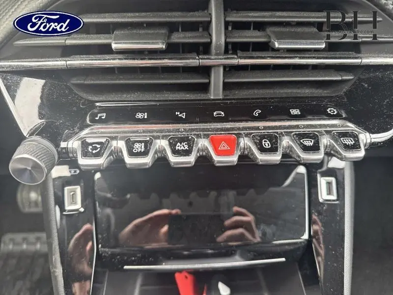 Tableau de bord noir avec rangée de boutons chromés et rouge au centre, vue rapprochée intérieure Peugeot 2008 blanc banquise