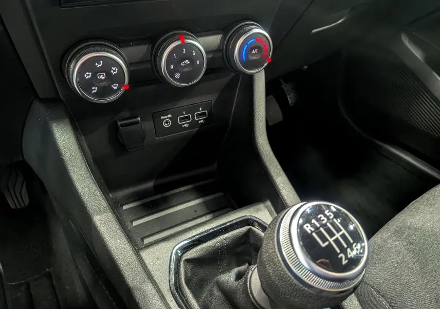Gros plan sur la console centrale de la Renault Clio V gris platine, mettant en valeur le levier de vitesse manuel et les commandes de climatisation.
