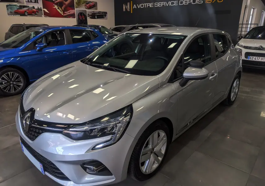 Renault Clio V gris platine vue 3/4 avant droit en showroom, avec phares LED et jantes alliage visibles.