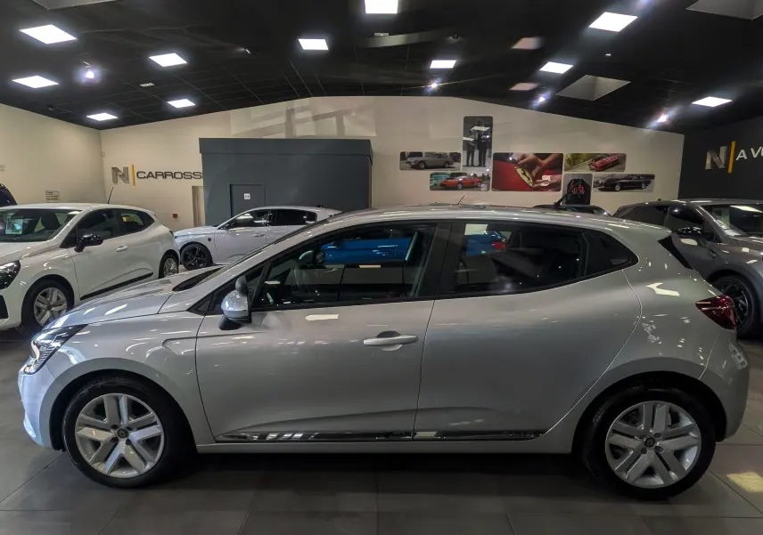 Profil côté gauche d'une Renault Clio V gris platine 2021 en showroom, avec jantes alliage et vitres teintées.