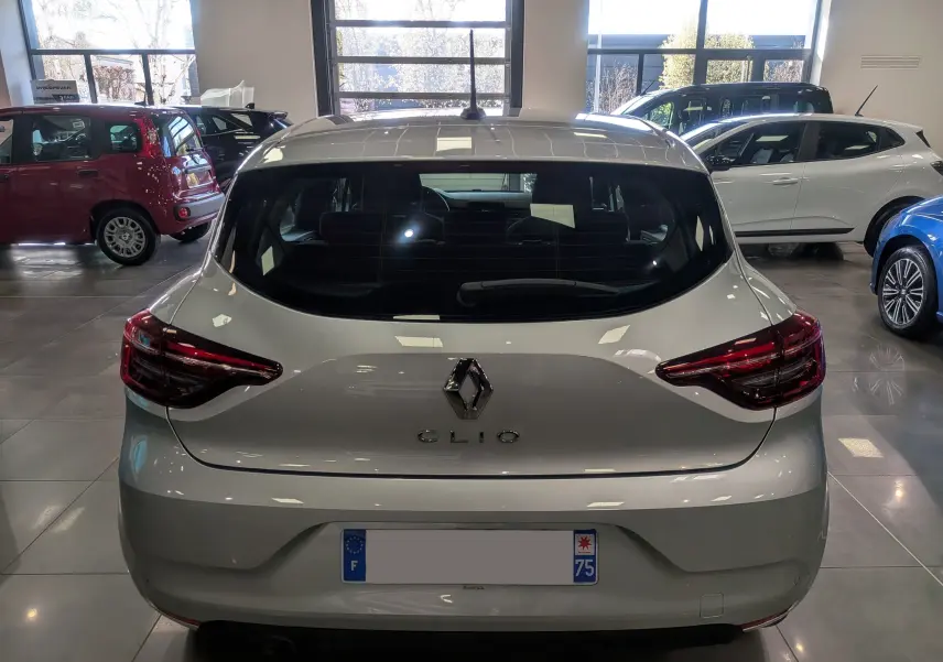 Vue arrière d'une Renault Clio V gris platine dans un showroom, avec feux arrière LED et logo central visible.