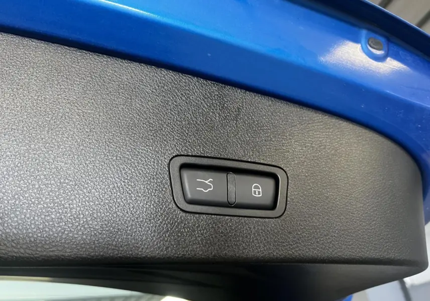 Gros plan sur le bouton d'ouverture et de verrouillage du hayon électrique, intérieur du coffre bleu visible.
