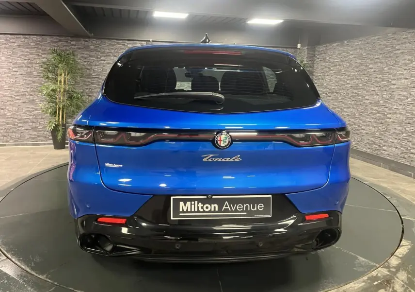 Vue arrière d'une Alfa Romeo Tonale bleu métallisé 2024 avec feux arrière LED et logo central sur fond noir brillant.