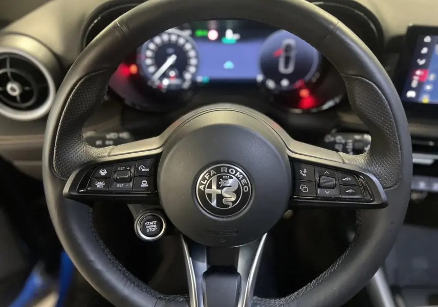 Gros plan sur le volant cuir noir d'Alfa Romeo Tonale 2024 avec commandes intégrées et logo central visible.