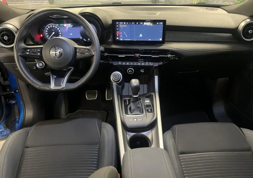 Vue intérieure avant de l'Alfa Romeo Tonale 2024, tableau de bord noir avec écran tactile et volant sport en cuir.