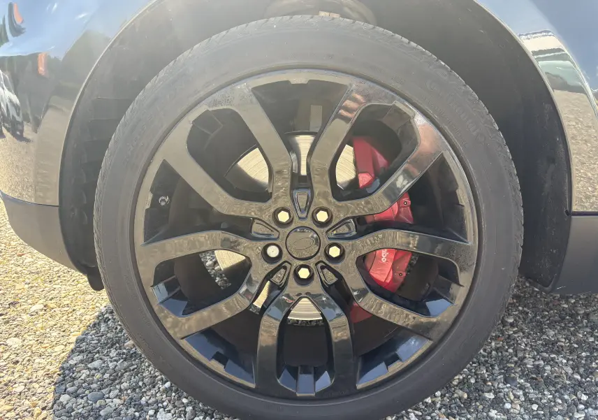 Gros plan sur la roue avant droite noire brillante d’un Range Rover Sport 2015 avec étrier de frein rouge Brembo.