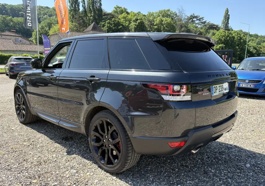Vue 3/4 arrière droite d'un Range Rover Sport noir brillant avec jantes noires et vitres teintées, stationné en extérieur.