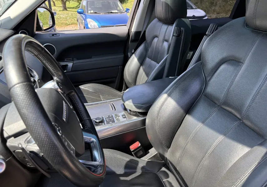 Intérieur du Range Rover Sport 2015 vu côté conducteur, sièges cuir noirs et console centrale avec commandes modernes.