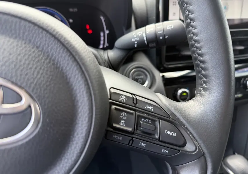 Gros plan sur le volant en cuir noir de la Toyota Yaris Cross 2024, avec commandes de régulateur de vitesse et aides à la conduite.