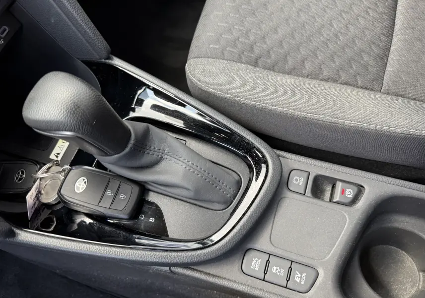 Vue rapprochée de la console centrale noire avec levier de vitesse automatique et clé Toyota sur siège tissu gris d'une Yaris Cross 2024.