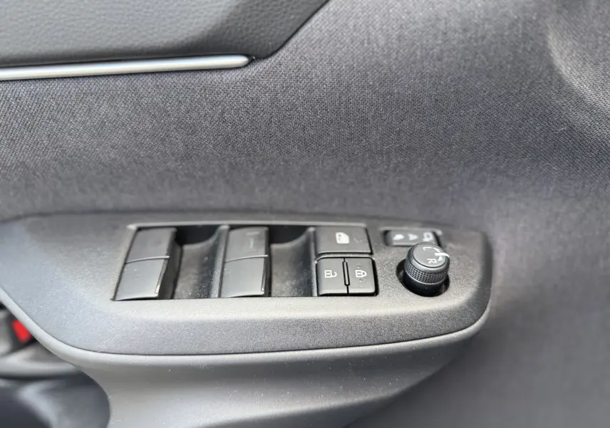 Gros plan sur les commandes de lève-vitres et réglage des rétroviseurs côté conducteur, intérieur noir du Toyota Yaris Cross 2024.