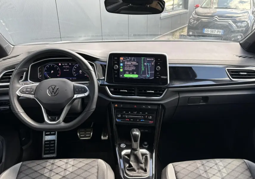 Vue intérieure avant du Volkswagen T-Roc 2025, tableau de bord noir avec écran tactile central et volant multifonction.