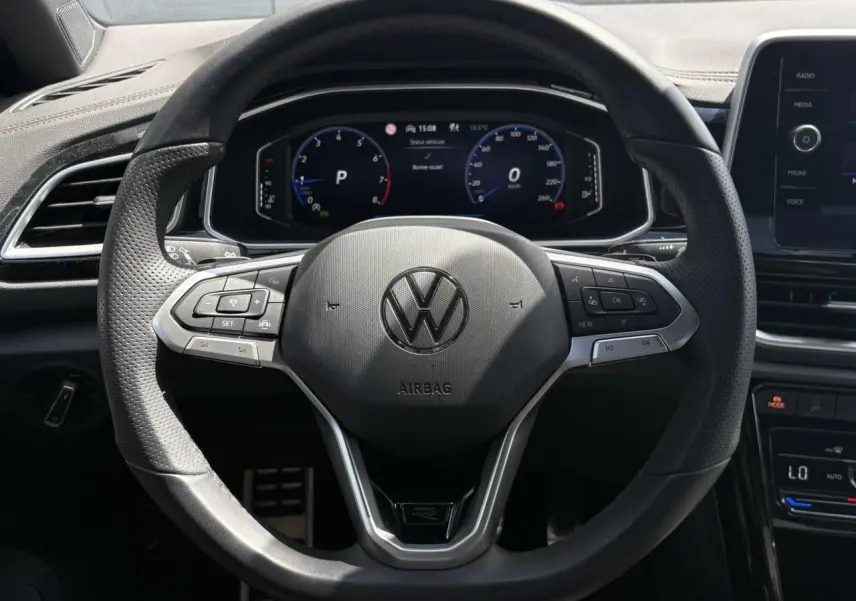 Vue rapprochée du volant sport multifonction R-Line noir du Volkswagen T-Roc 2025 avec tableau de bord digital en arrière-plan.
