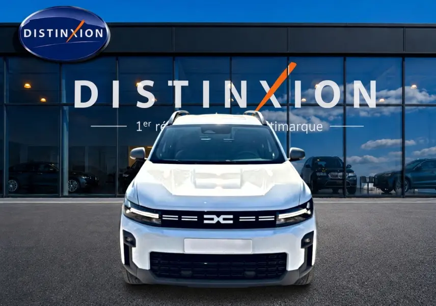 Vue avant d'un Dacia Bigster blanc 2026 avec calandre noire et barres de toit visibles devant une vitrine Distinxion.