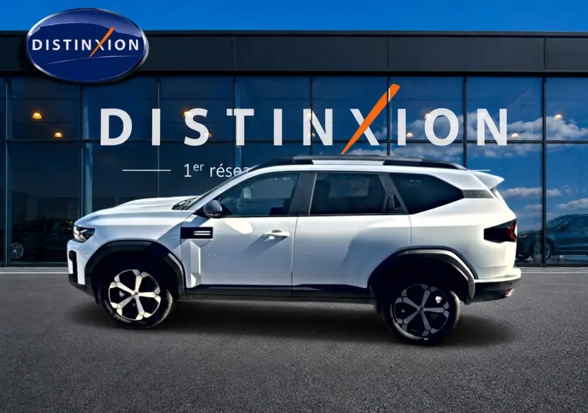 Profil droit du SUV blanc Dacia Bigster 2026 avec jantes alu et barres de toit devant une vitrine Distinxion.