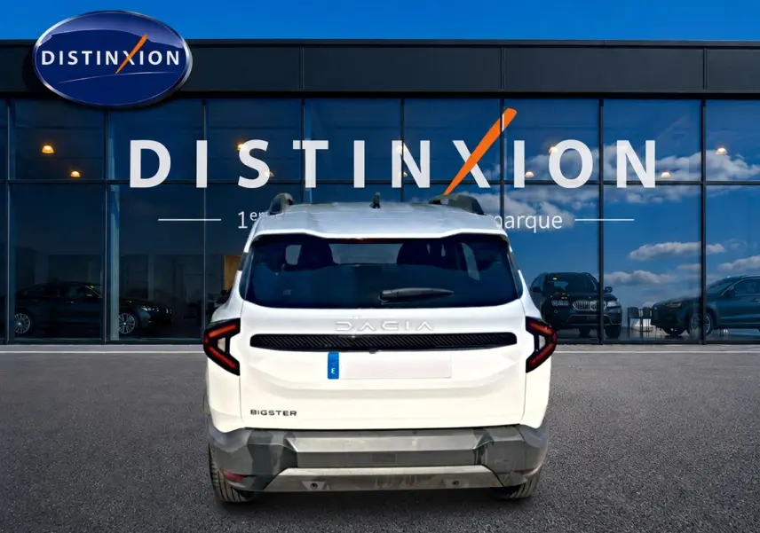 Vue arrière d'un Dacia Bigster blanc garé devant une vitrine avec logo Distinxion, feux arrière LED en forme de C.