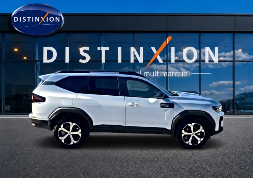 Profil droit du Dacia Bigster blanc 2026 avec jantes alu et barres de toit devant une vitrine Distinxion.