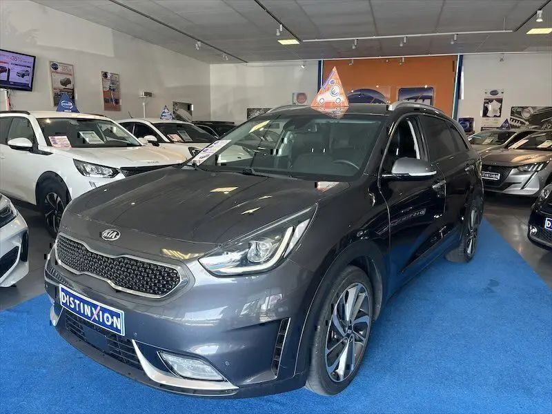 KIA Niro hybride gris galène en 3/4 avant droit, avec jantes alliage et calandre distinctive en showroom.
