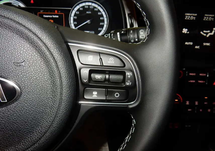 Gros plan sur le volant noir de la Kia Niro hybride 2019, montrant les commandes de régulateur et tableau de bord éclairé.
