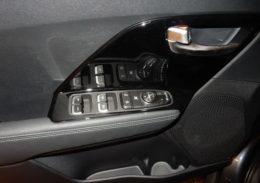 Détail de la porte côté conducteur du Kia Niro gris galène, montrant les commandes des vitres, rétroviseurs et la poignée intérieure.