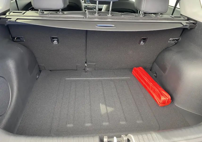 Coffre arrière vu de l'intérieur d'un Kia Niro gris galène, avec un triangle de signalisation rouge rangé à droite.