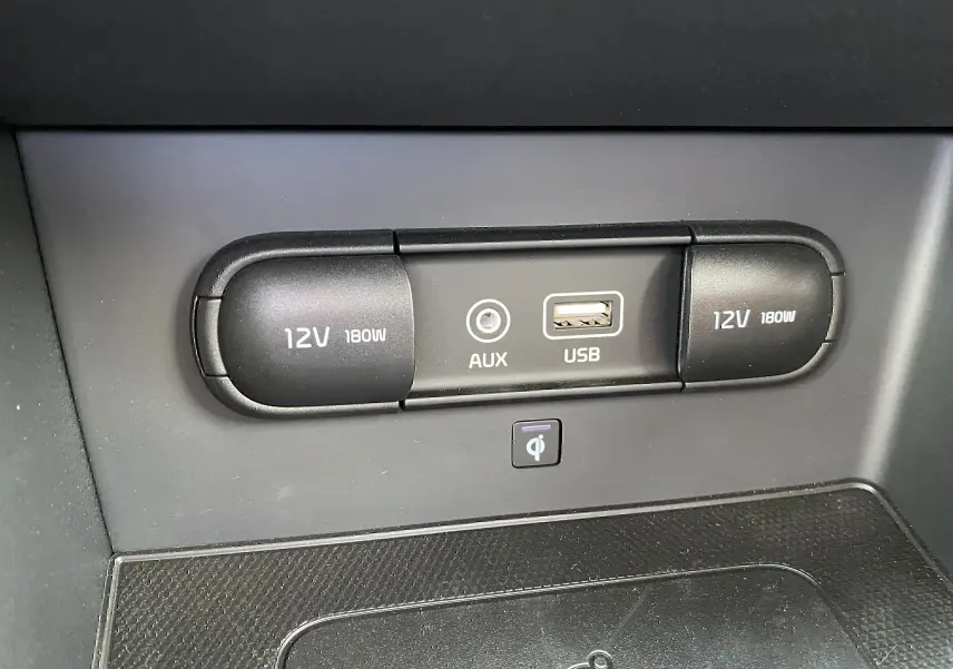 Gros plan sur la console centrale du Kia Niro hybride 2019, montrant prises 12V, port AUX et USB, avec surface de recharge sans fil.