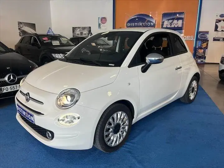 Vue 3/4 avant d'une FIAT 500 blanche avec jantes alliage et rétroviseurs chromés en showroom.