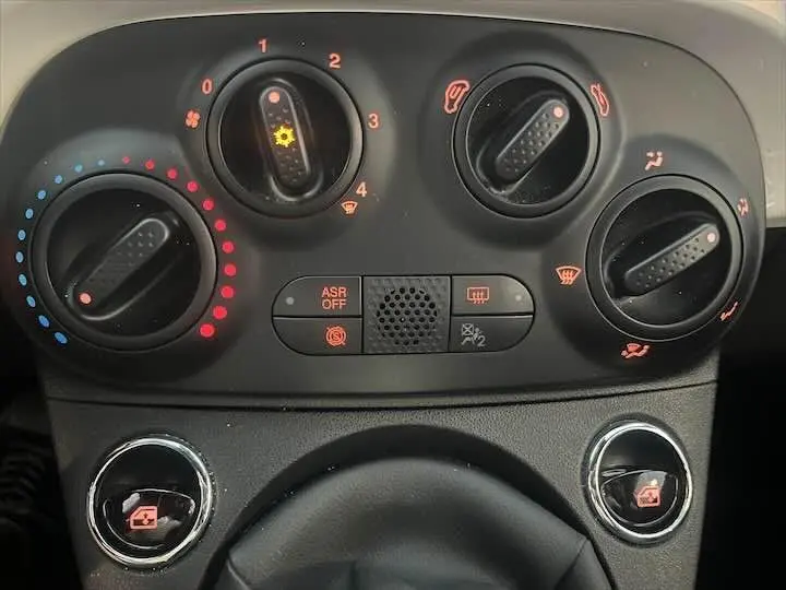 Gros plan sur les commandes de climatisation et ventilation du tableau de bord noir de la Fiat 500 blanche 2023.