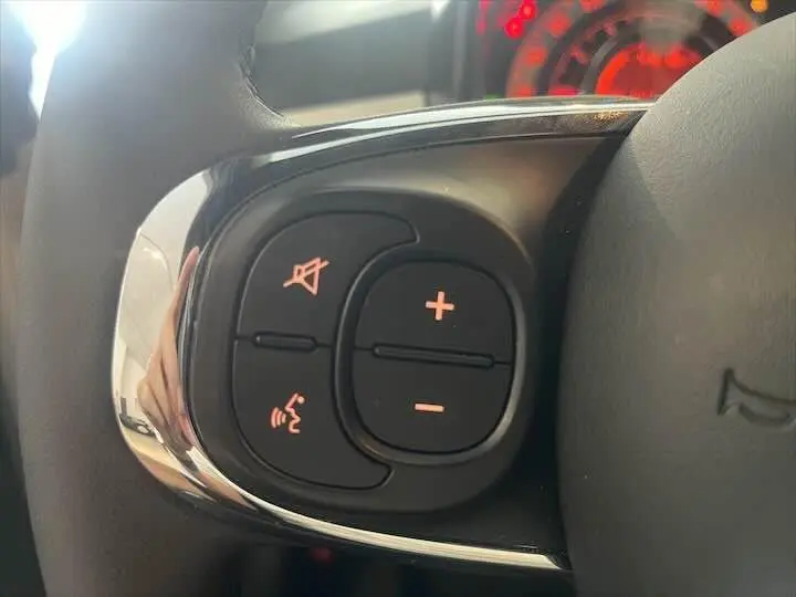 Gros plan sur les commandes de volume et de sourdine au volant d'une Fiat 500 blanche, tableau de bord en arrière-plan rouge.