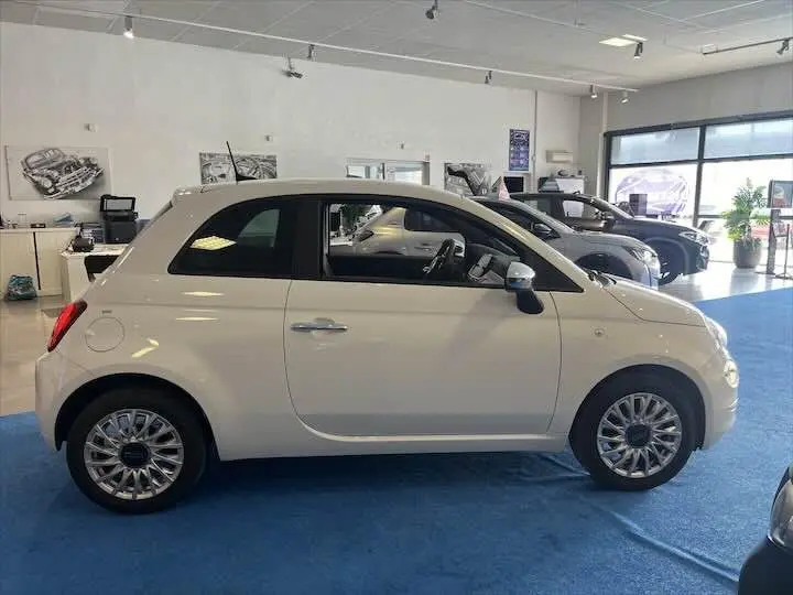 Profil côté gauche d'une FIAT 500 blanche 2023 en showroom, avec jantes alliage et toit noir contrastant.