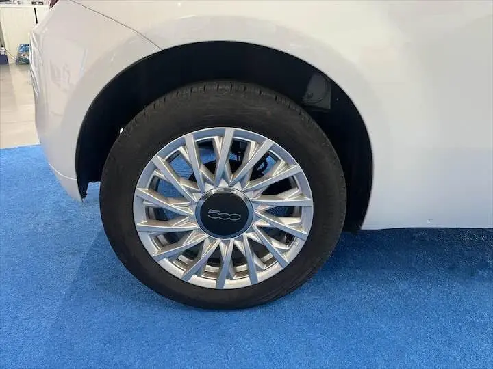 Gros plan sur la roue avant gauche blanche d'une FIAT 500 2023 avec jante argentée au design étoilé.