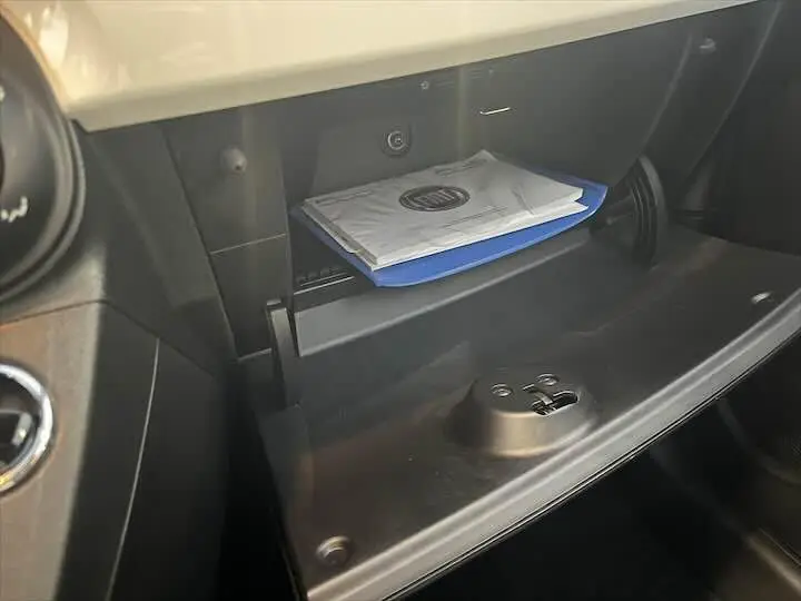Gros plan sur la boîte à gants ouverte de la Fiat 500 blanche 2023, avec manuel visible à l'intérieur.