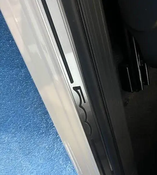 Gros plan sur la plaque de seuil de porte côté gauche blanche d'une Fiat 500 avec logo 500 noir.