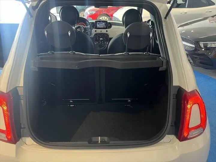 Coffre ouvert d'une FIAT 500 blanche vue de l'arrière, avec intérieur noir et tableau de bord visible à travers les sièges.
