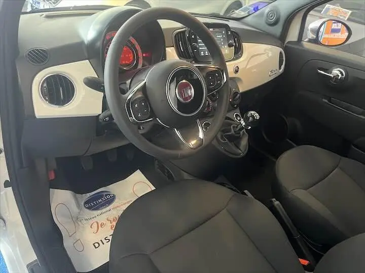 Vue intérieure côté conducteur de la Fiat 500 blanche 2023, tableau de bord beige et volant multifonction noir.