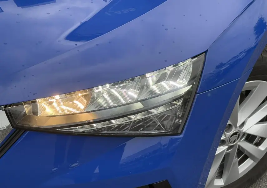 Gros plan sur le phare avant droit et la jante argentée d'une SKODA SCALA TSI 110 DSG Ambition bleu Energy 2024.