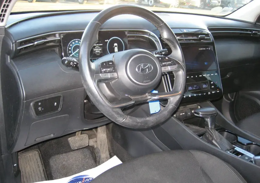Vue intérieure du tableau de bord et volant noir du Hyundai Tucson III hybride, avec écran tactile et levier de vitesse automatique.