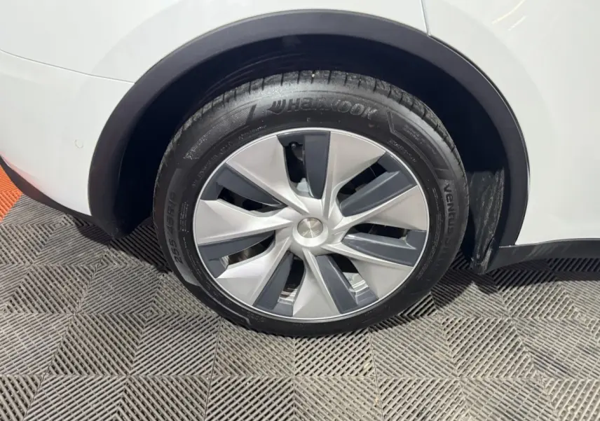 Gros plan sur la roue arrière droite d'une Tesla Model Y blanche, mettant en valeur la jante moderne et le pneu Hankook.