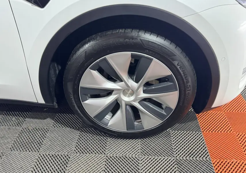 Gros plan sur la roue avant gauche d'une Tesla Model Y blanche, avec jante aérodynamique et pneu Hankook.