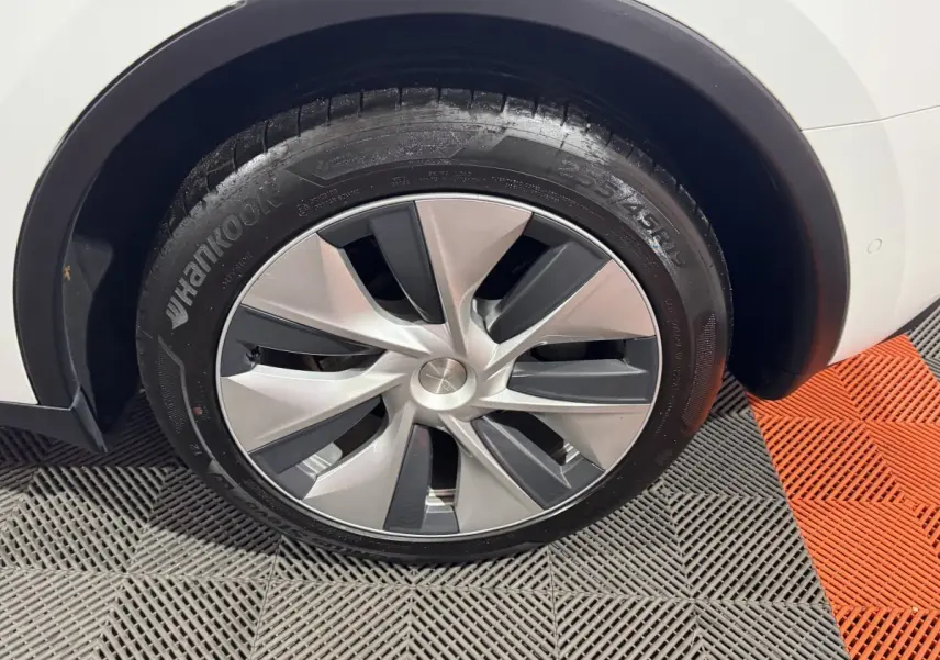 Gros plan sur la roue avant droite d'une Tesla Model Y blanche, jante aérodynamique grise et noire.