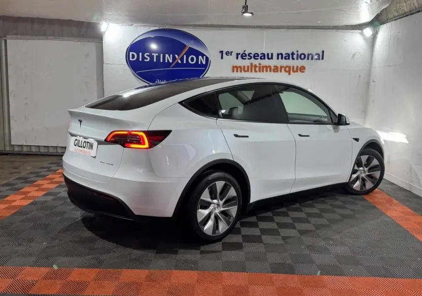 Tesla Model Y blanc en 3/4 arrière droit dans un showroom avec feux arrière LED allumés.