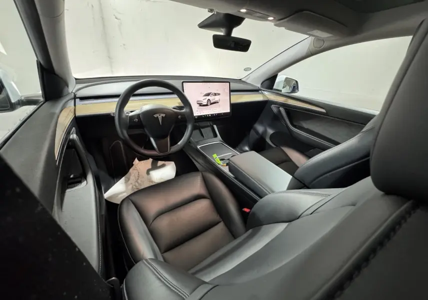 Intérieur noir de Tesla Model Y 2022, vue depuis l'arrière droit, avec tableau de bord minimaliste et écran tactile central.