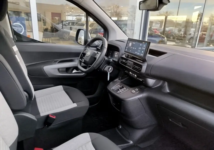 Vue intérieure côté conducteur du Citroën Berlingo 2025 avec sièges gris, tableau de bord noir et écran tactile central.
