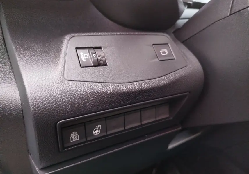 Gros plan sur les commandes noires du tableau de bord côté gauche du Citroën Berlingo Kaolin White 2025, avec réglage des phares et chauffage de volant.