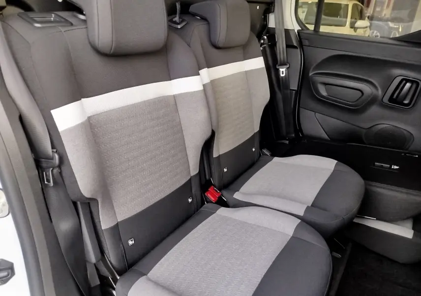 Vue latérale des sièges arrière gris clair et foncé du Citroën Berlingo 2025, avec ceinture de sécurité et porte noir visible.